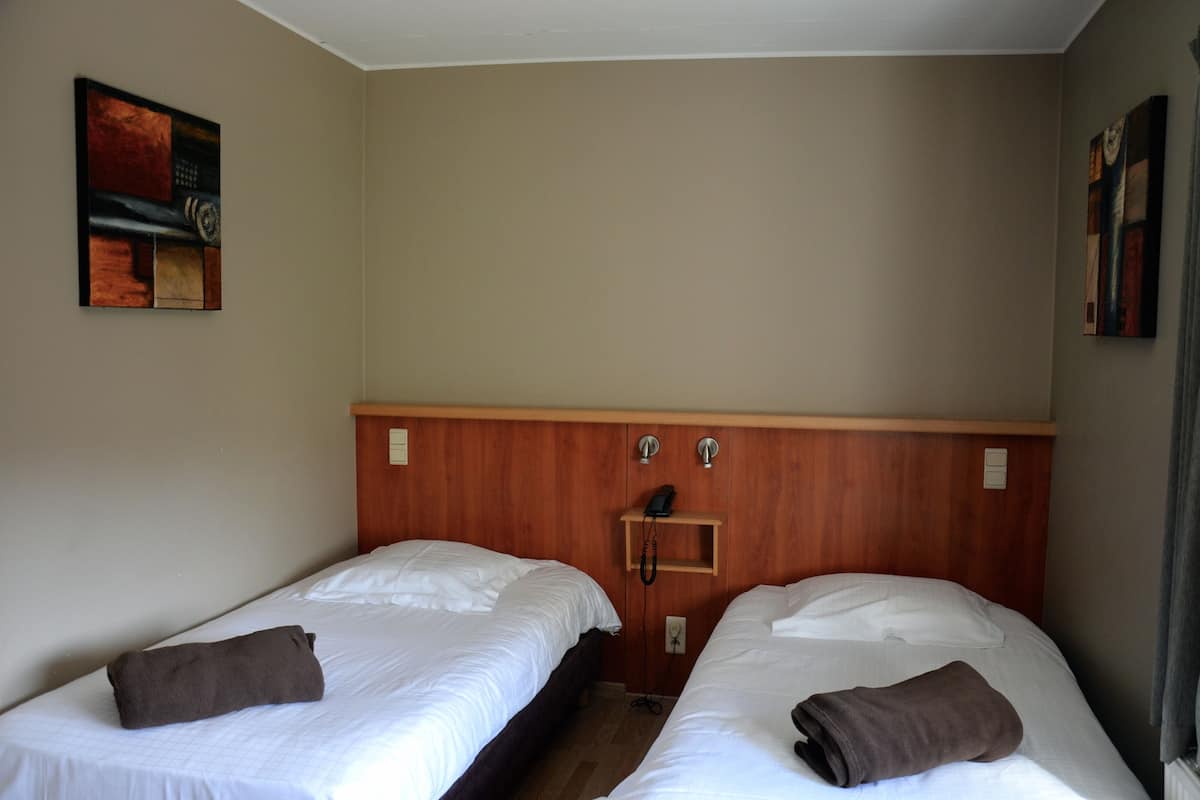 A hotel room with two single beds, a wooden headboard, a telephone, and a small shelf.