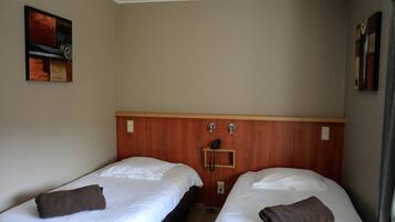 Een hotelkamer met twee enkele bedden, een houten hoofdbord, een telefoon en een klein plankje.
