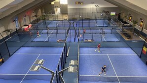 Impianto indoor polivalente per tennis con diverse piste, zone con posti a sedere e tabellone segnapunti.