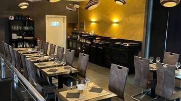 A modern restaurant with a long dining area, black and white striped pendant lights, and a bar area in the background.
