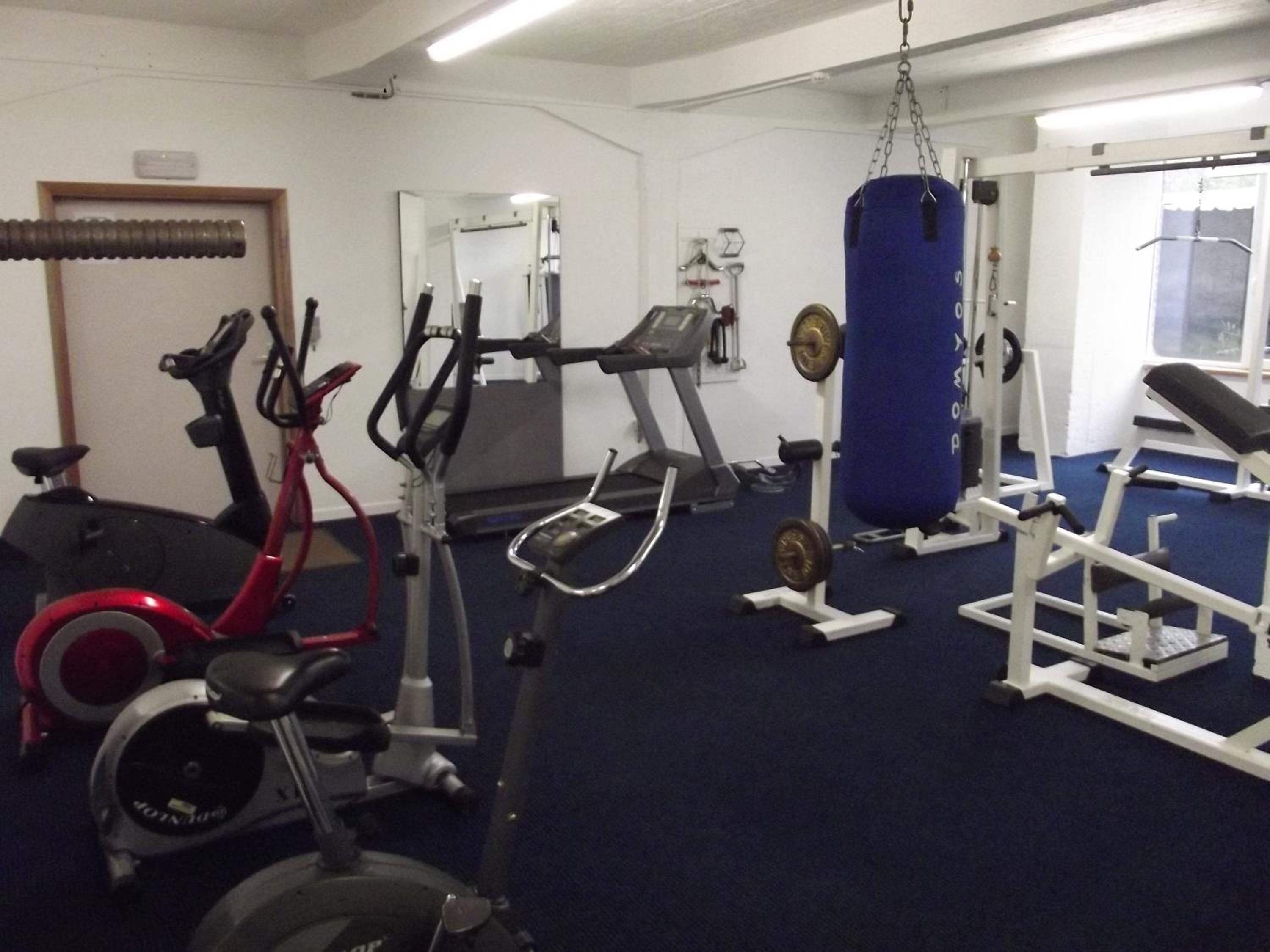 Een sportschool met hometrainers, loopband, krachttoestellen en een bokszak.