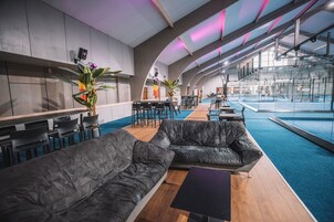 Un área interior de piscina moderna con un sofá de cuero negro, mesas y sillas de madera.