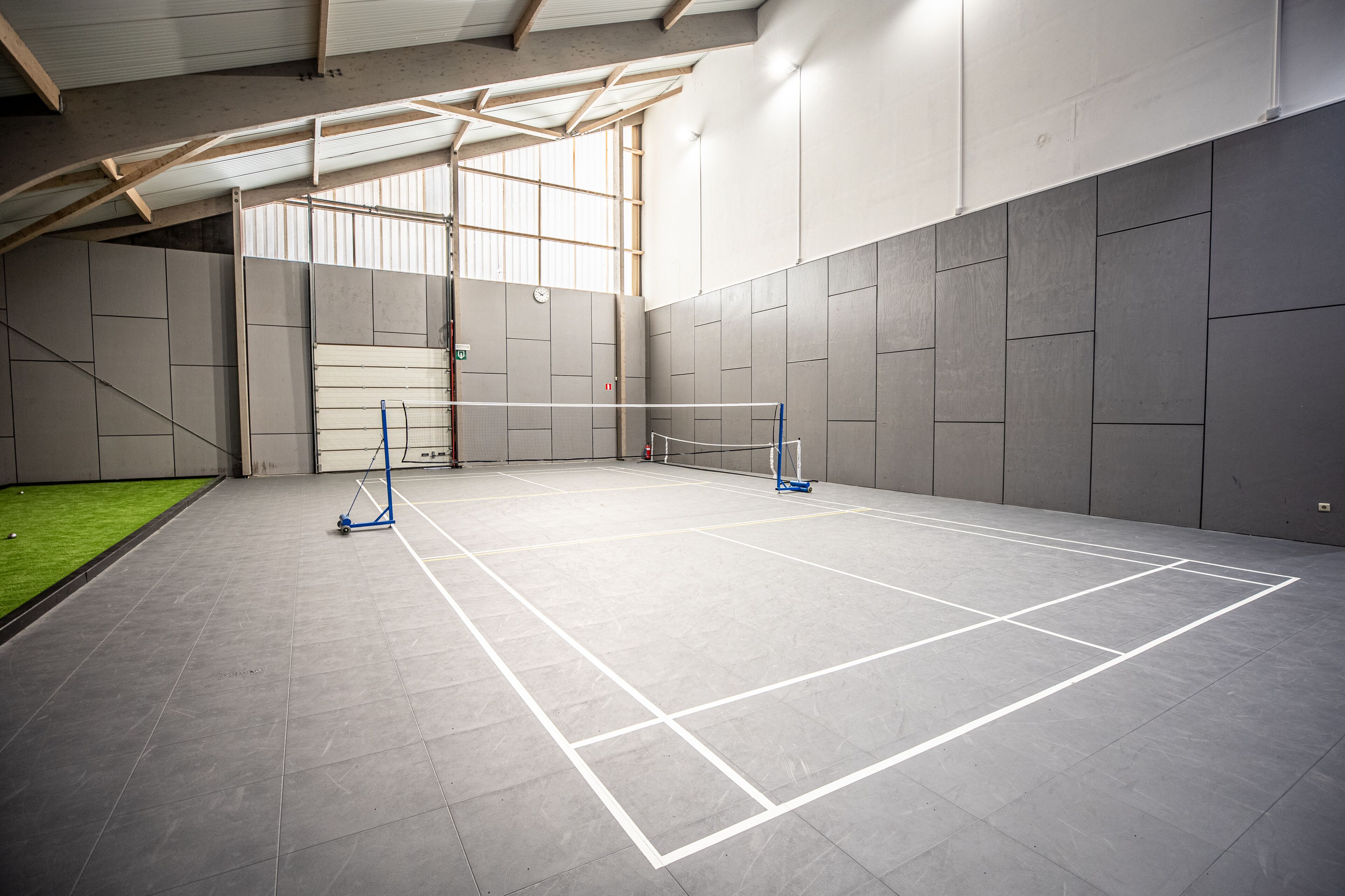 Una cancha de tenis cubierta con red, paredes y una zona de césped artificial verde.