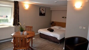 Una camera d'albergo con un letto, un tavolo di legno con sedie, una pianta in vaso e una finestra con tende.