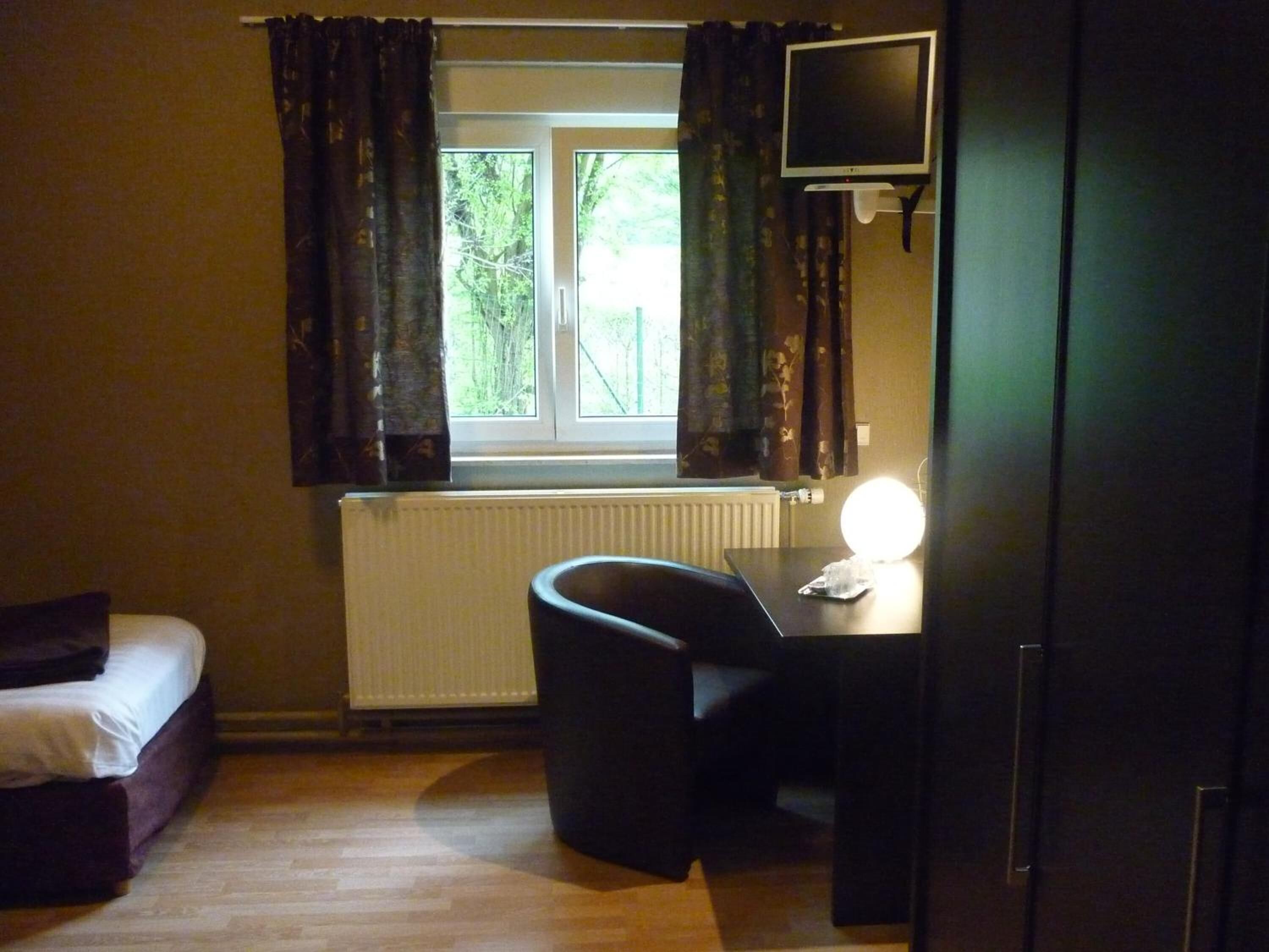 Een kleine kamer met een bed, een bureau met een computerscherm, een stoel en een radiator.