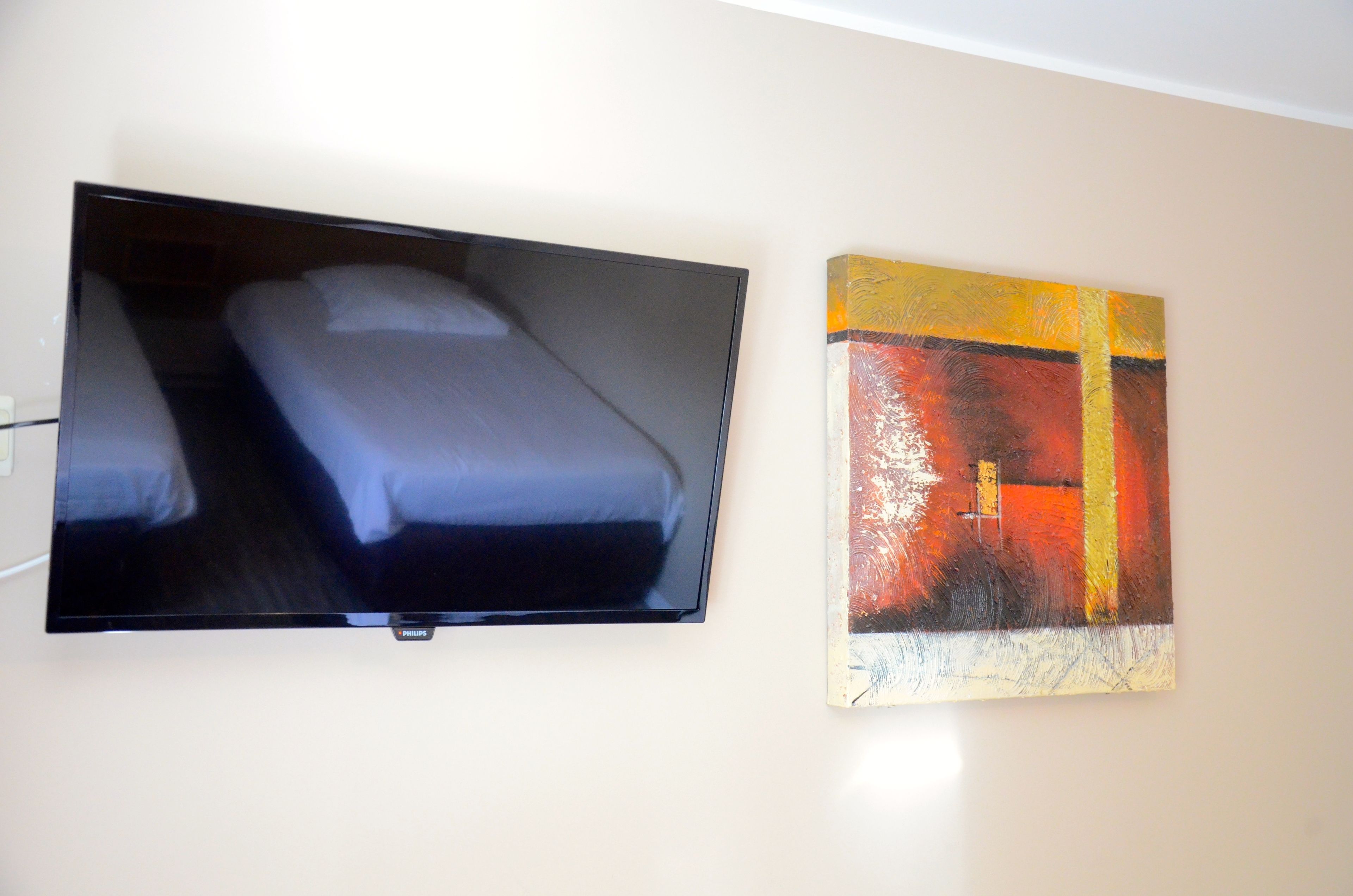 Cama com televisão na parede e um quadro.