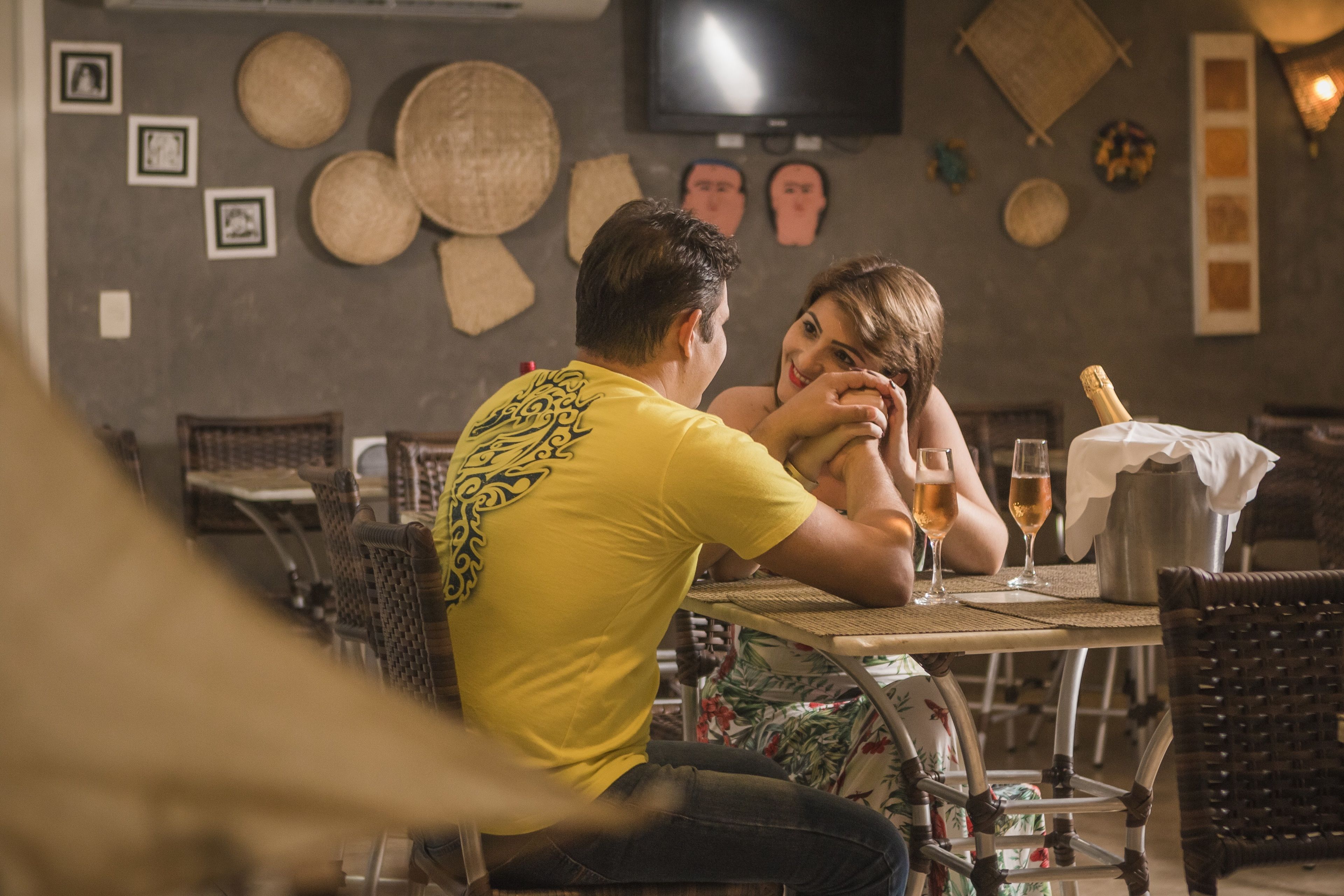 Un interior de restaurante con mobiliario de mimbre, un televisor en la pared y una botella de champán sobre la mesa.