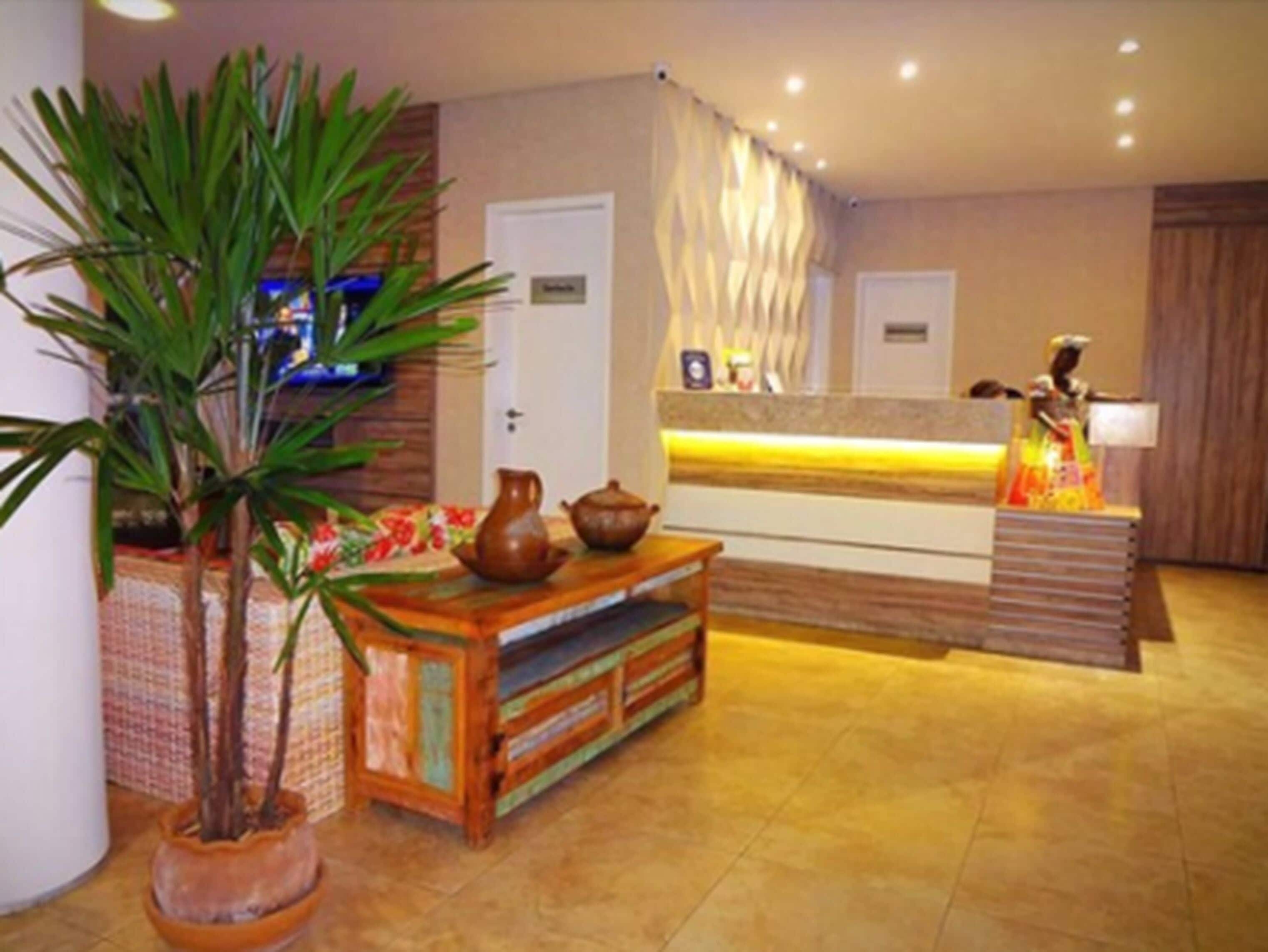 Un espace d’accueil comprenant un comptoir de réception en bois, une plante en pot, un téléviseur et un présentoir avec un objet décoratif.