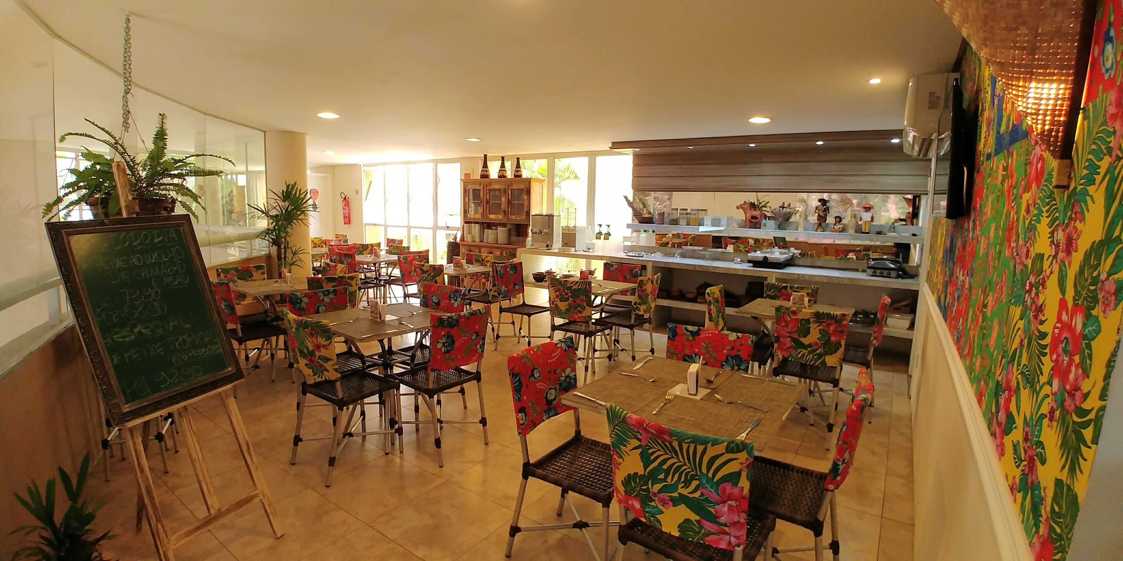 Un restaurante con varias mesas y sillas, un menú en una pizarra y una zona de cocina.