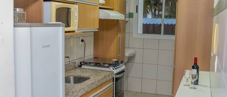 A compact kitchen with wooden cabinets, a microwave, a stove, and a window with a view of palm trees.