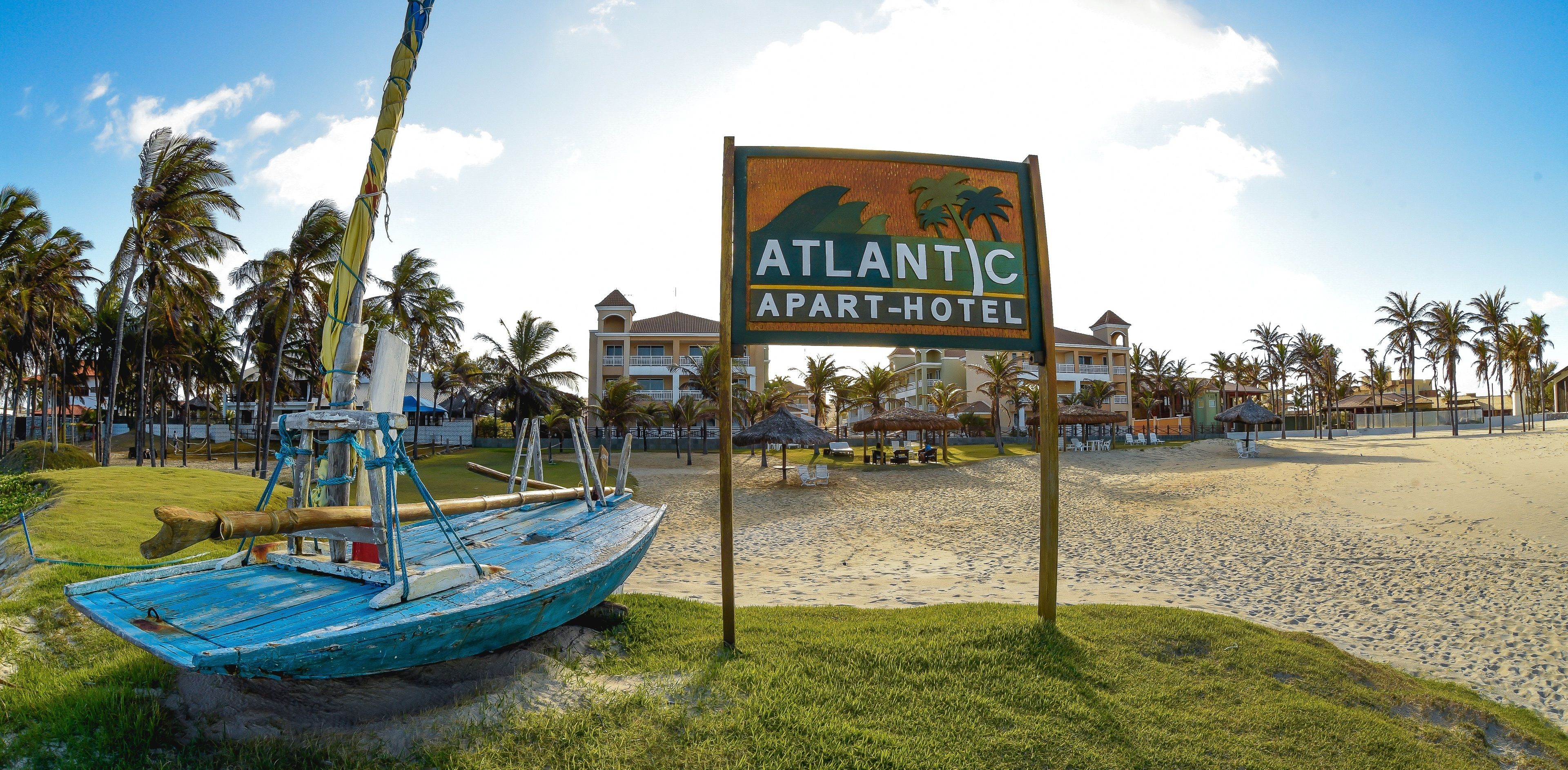 A beach with a sign for the Atlantic Apart-Hotel, palm trees, and a blue boat.