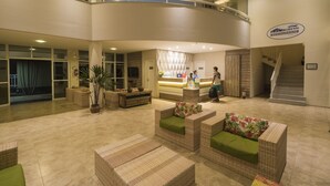 A spacious lobby with wicker furniture, a reception desk, and a staircase leading to upper floors. - Atlantic Palace Apart-Hotel (Aquiraz)