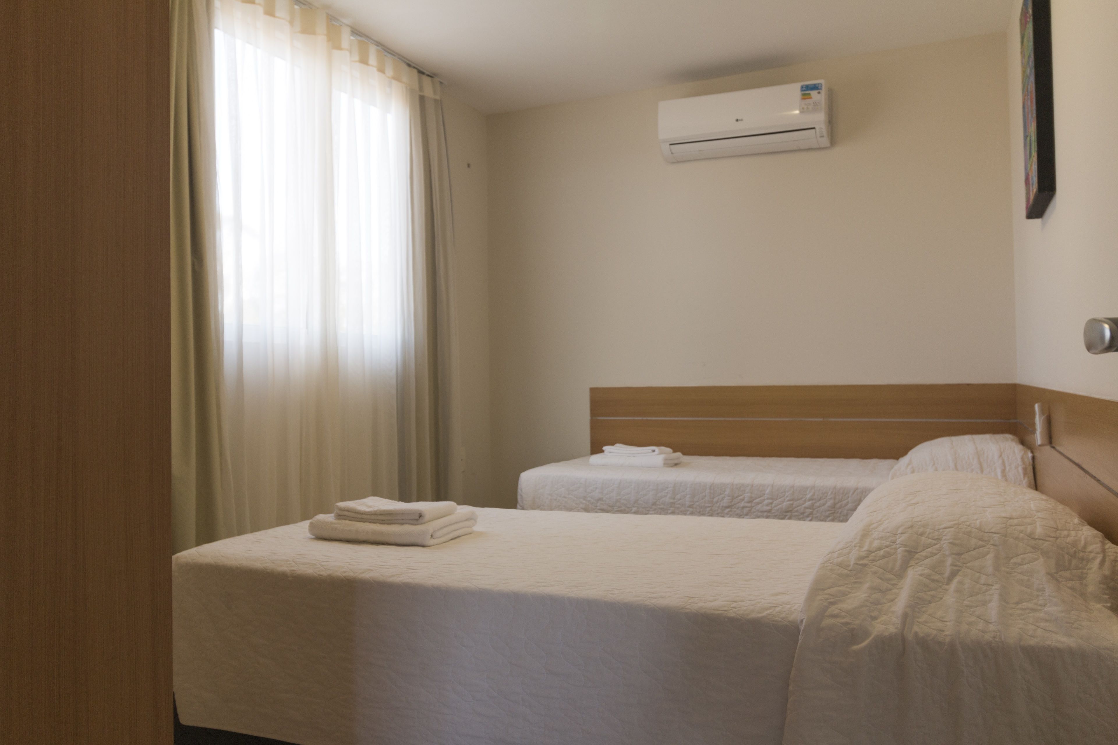 A hotel room with two beds, a window with curtains, an air conditioning unit on the wall, and a framed picture on the wall.