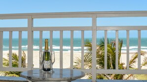A balcony with a table featuring a bottle of champagne and a glass, overlooking a beach with palm trees and the ocean. - Atlantic Palace Apart-Hotel (Aquiraz)