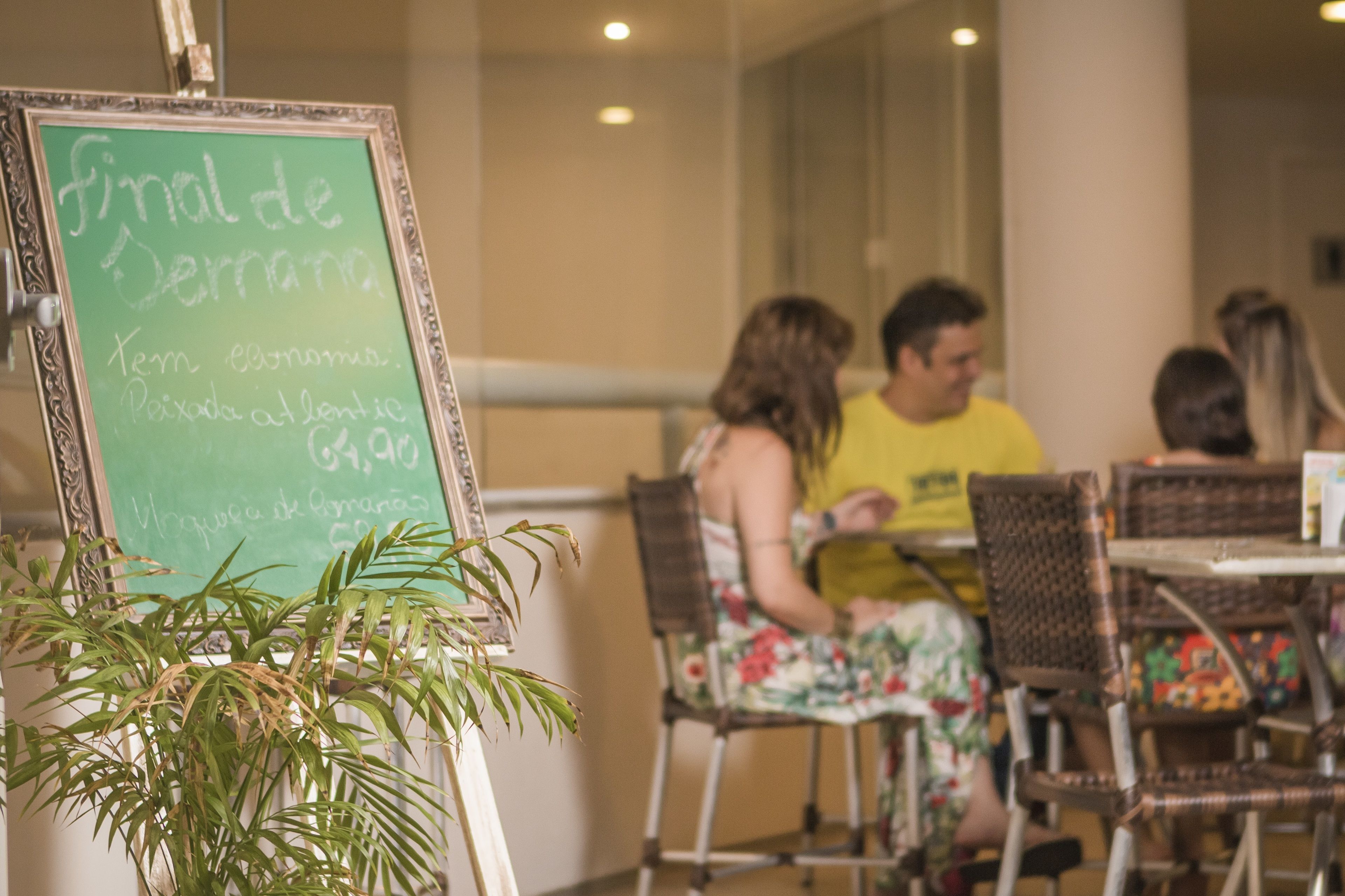 A restaurant with a chalkboard menu, wicker furniture, and a potted plant.