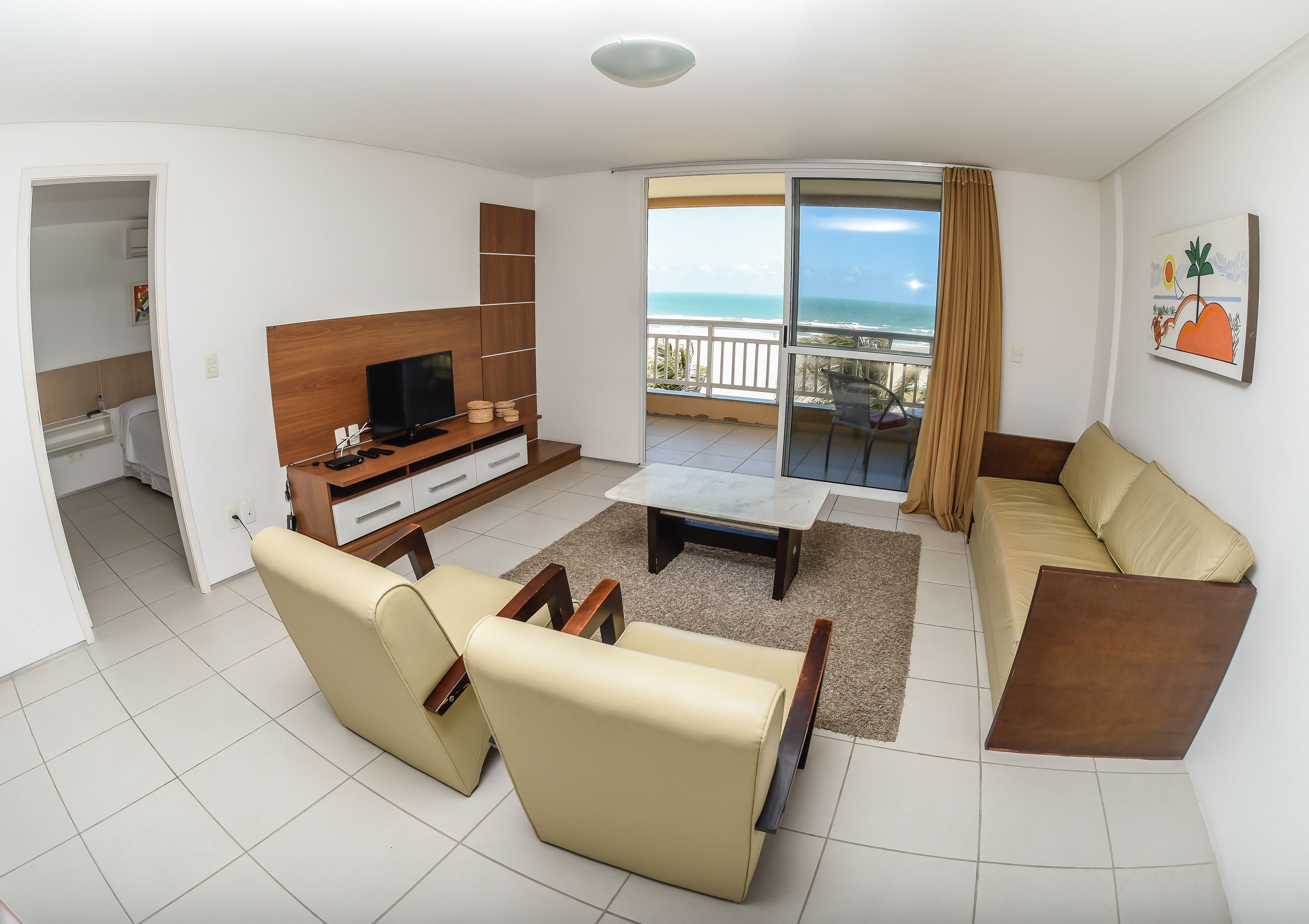 A modern living room with a sofa, TV, and a balcony with a view of the ocean.