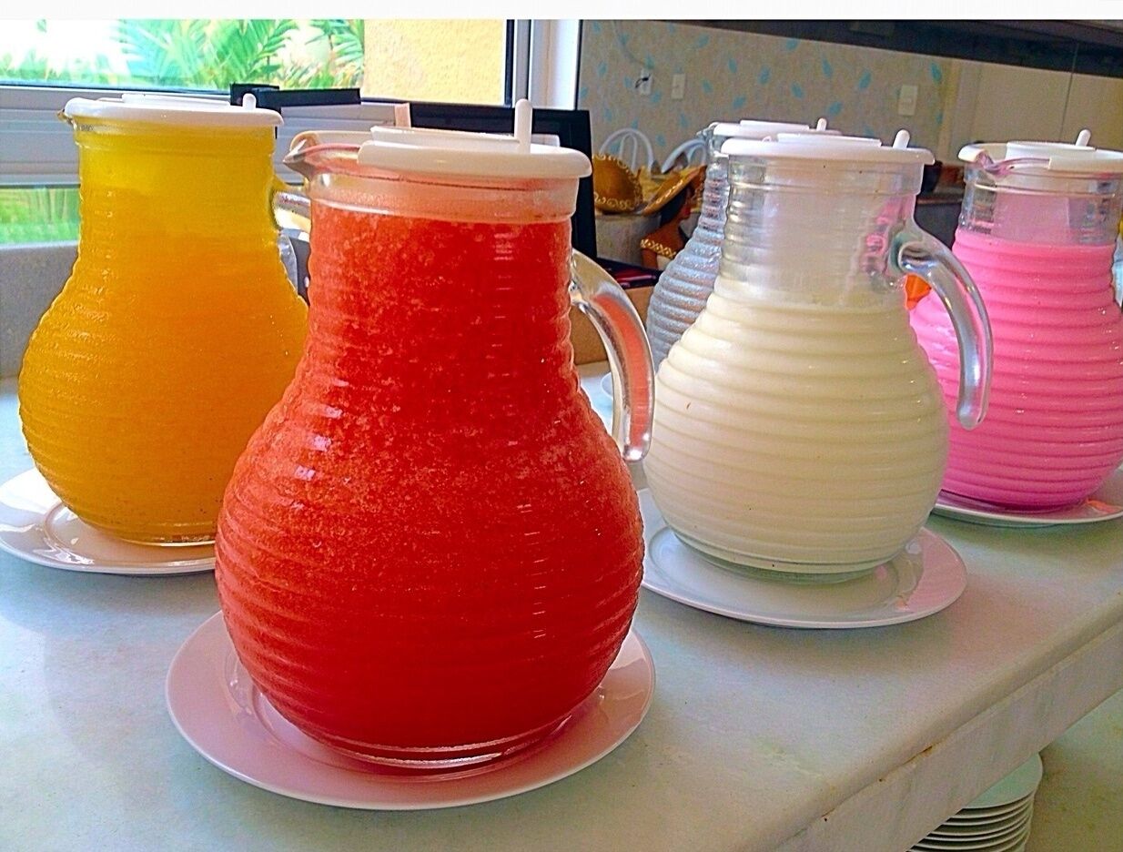 Four colorful pitchers on a counter, each with a different color: yellow, red, white, and pink.