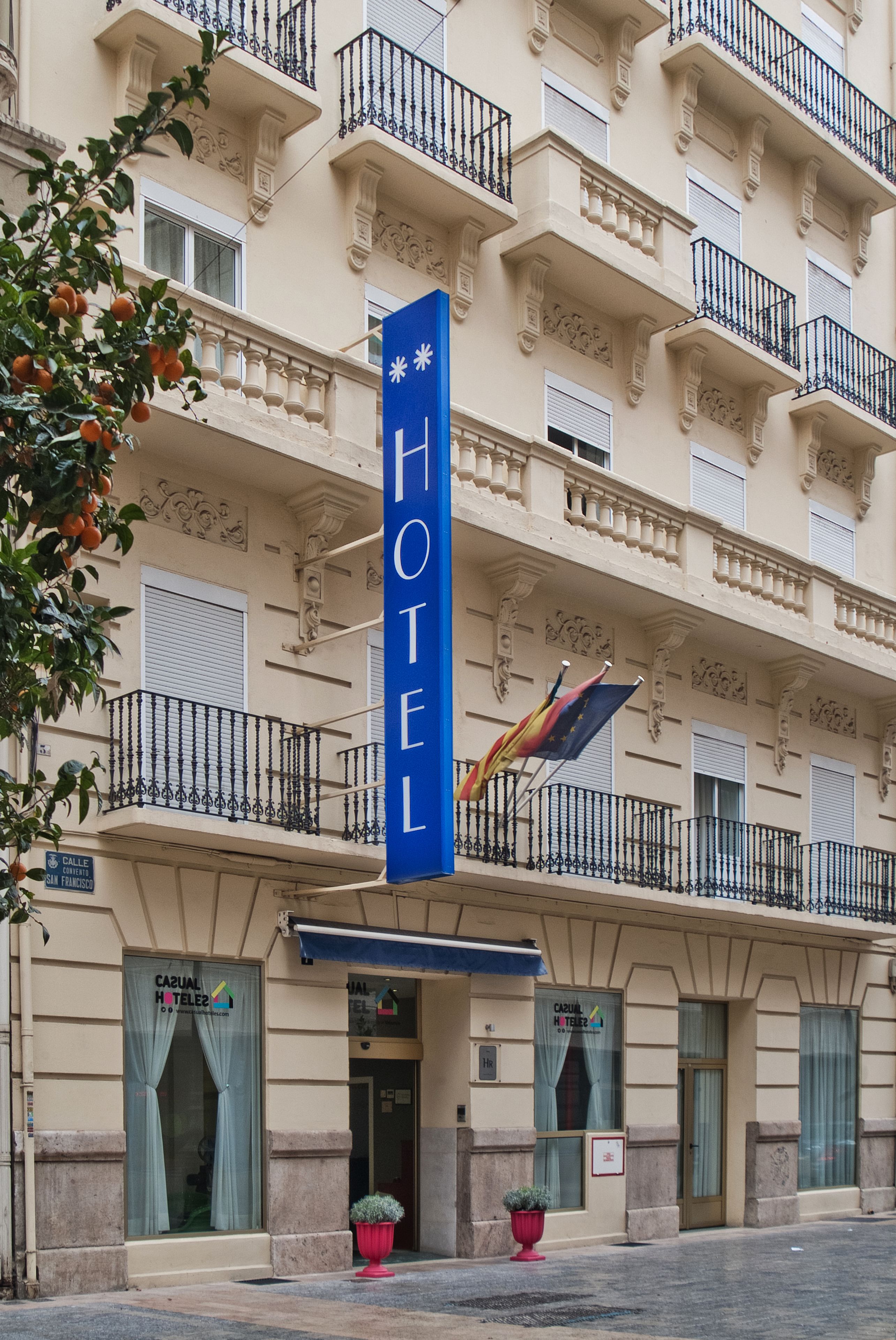 Facciata di un hotel con balconi, insegna blu e bandiere.