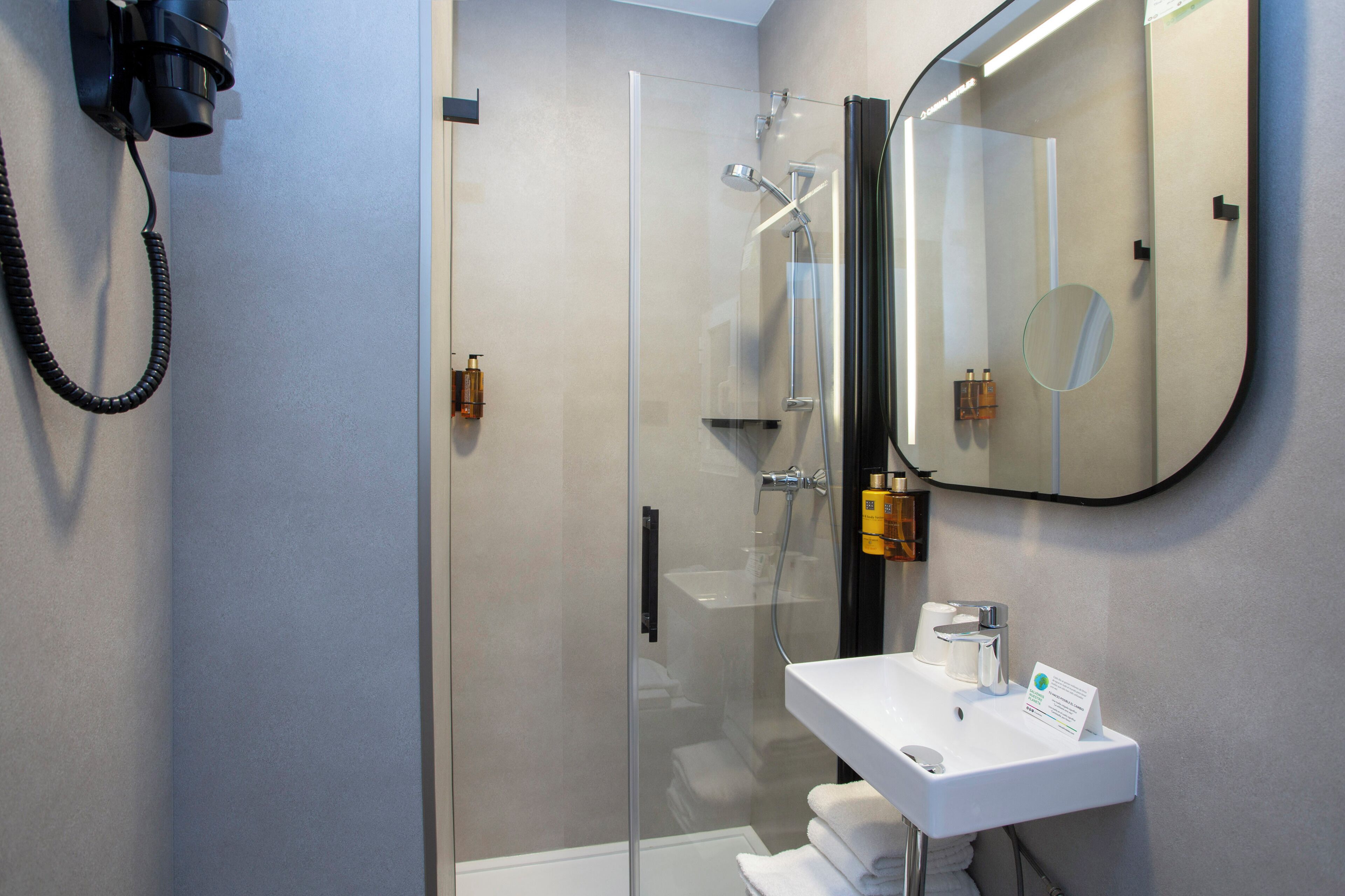 Un baño moderno con ducha de vidrio, lavamanos blanco y un espejo grande.
