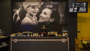 Zona de recepción con una gran foto en blanco y negro, un televisor y un mostrador con diversos alimentos y una planta pequeña.