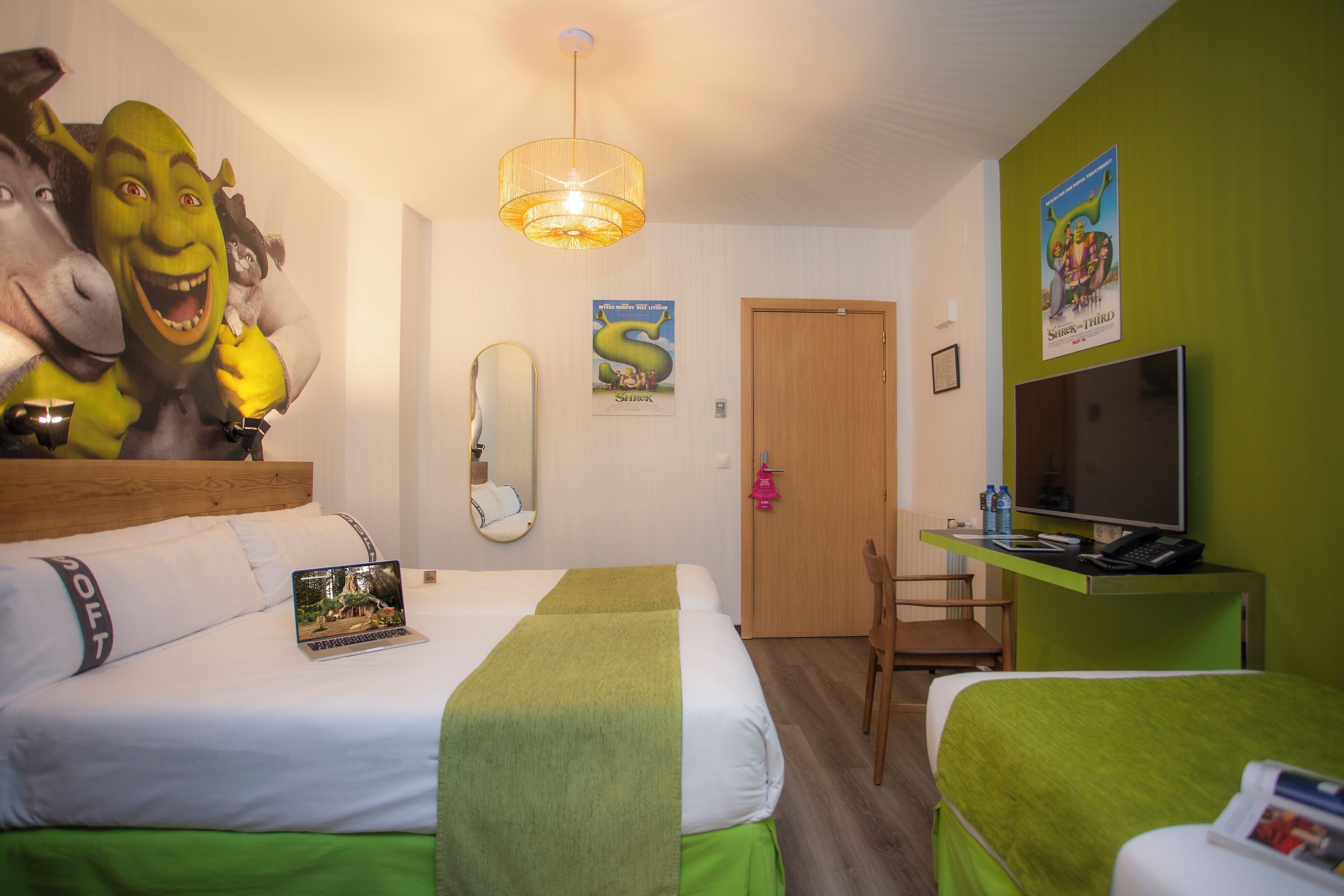 A hotel room with two beds, a television, a desk with a computer, and a mirror.