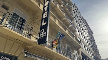 A hotel building with balconies, a sign reading "Hotel Casual del Cine Valencia," and flags.