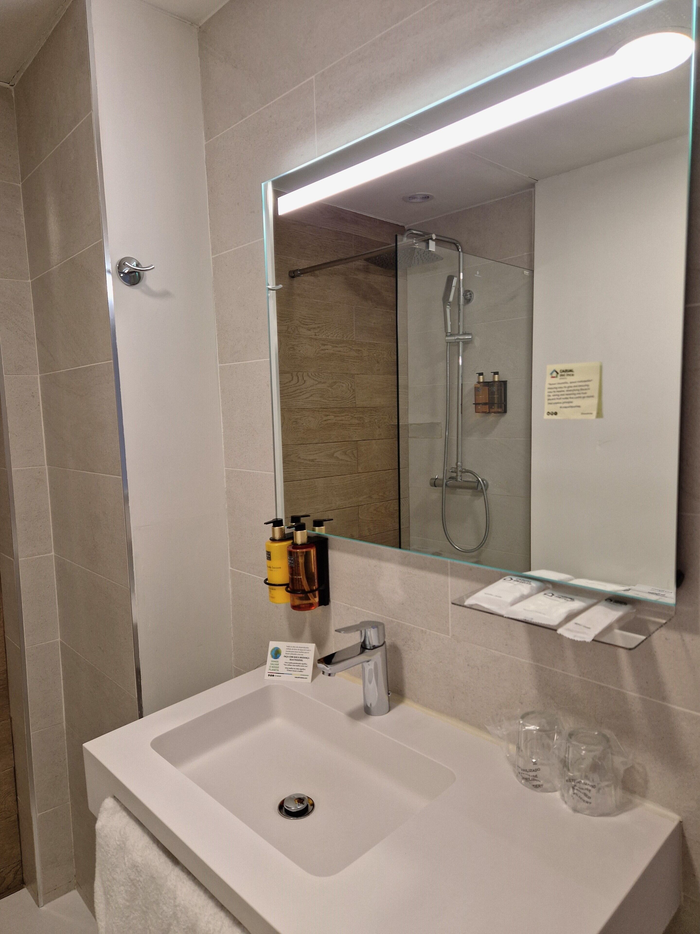A modern bathroom with a large mirror, a glass shower enclosure, a white sink, and toiletries on the wall.