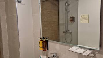 A modern bathroom with a large mirror, a glass shower enclosure, a white sink, and toiletries on the wall.