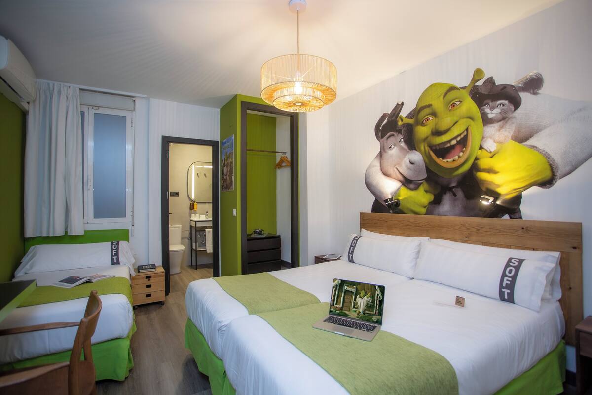 Hotellihuone, jossa on kaksi sänkyä, suuremmalla sängyllä kannettava tietokone ja seinällä suuri seinämaalaus, jossa on kuvattuna animoituja hahmoja.