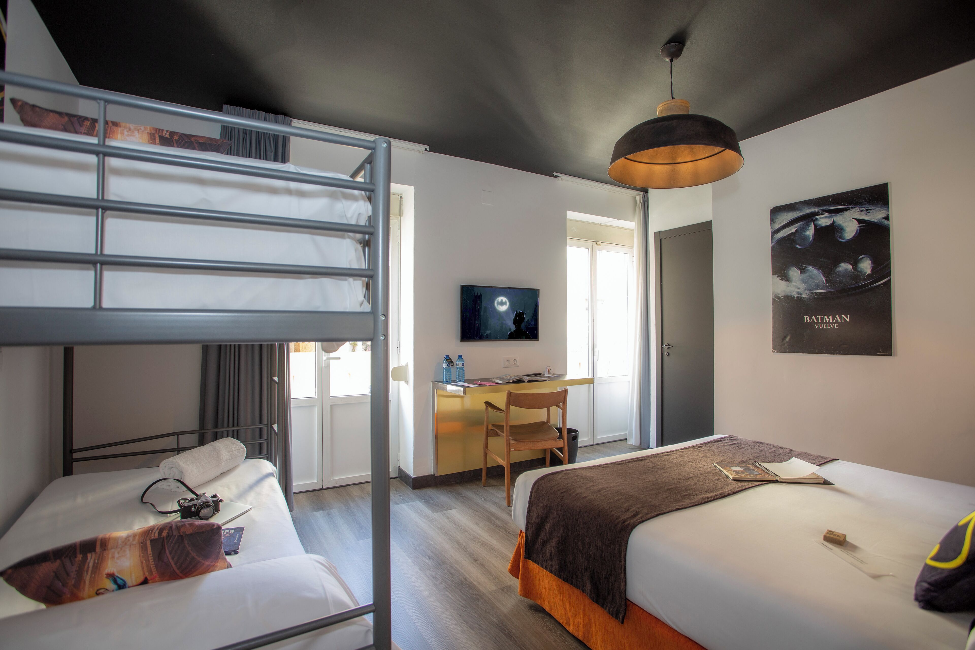 A hotel room with a bunk bed, a desk with a chair, a television, and a Batman poster on the wall.
