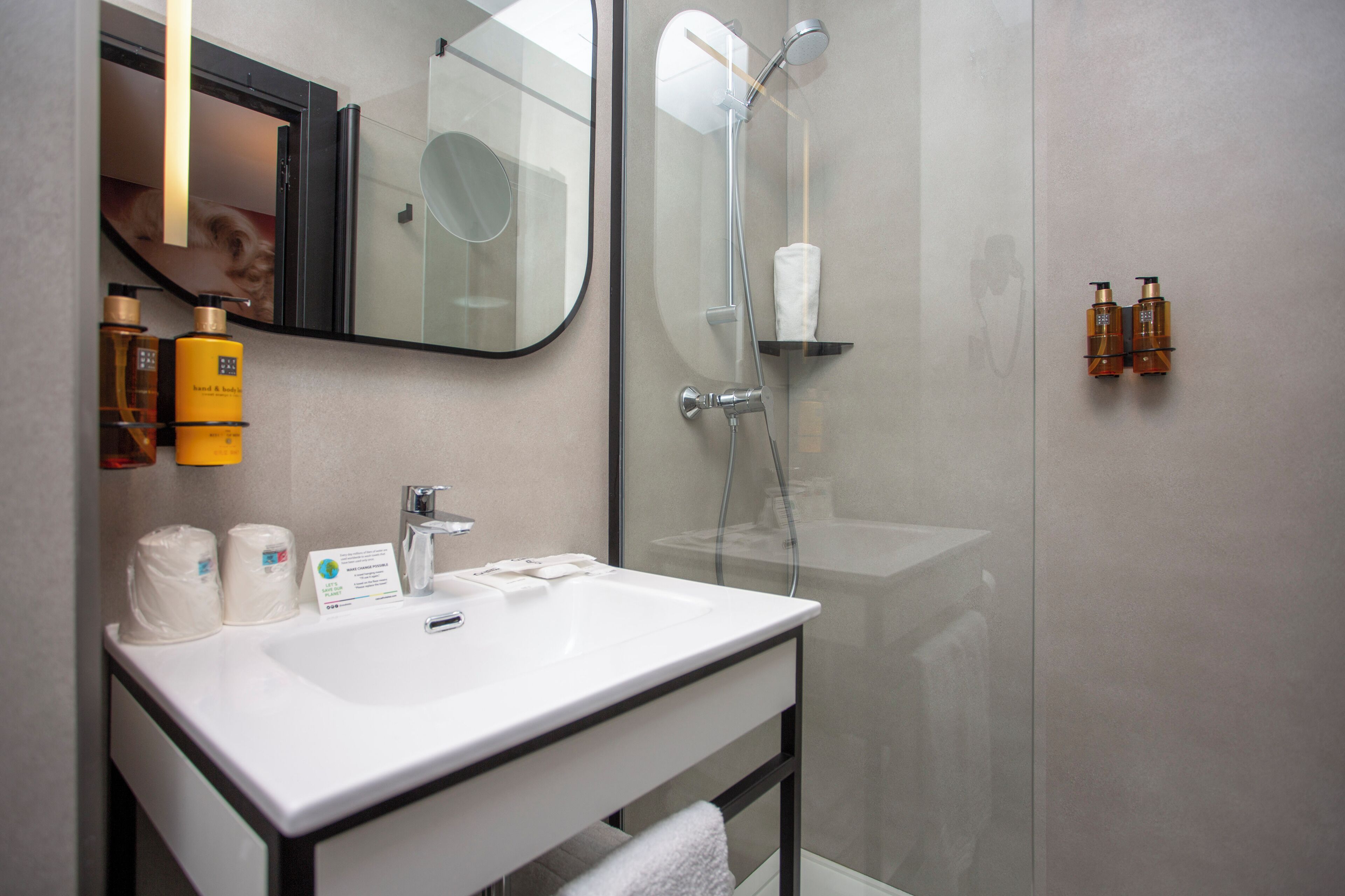 Un baño moderno con un lavamanos blanco, un espejo y una ducha con mampara de vidrio.