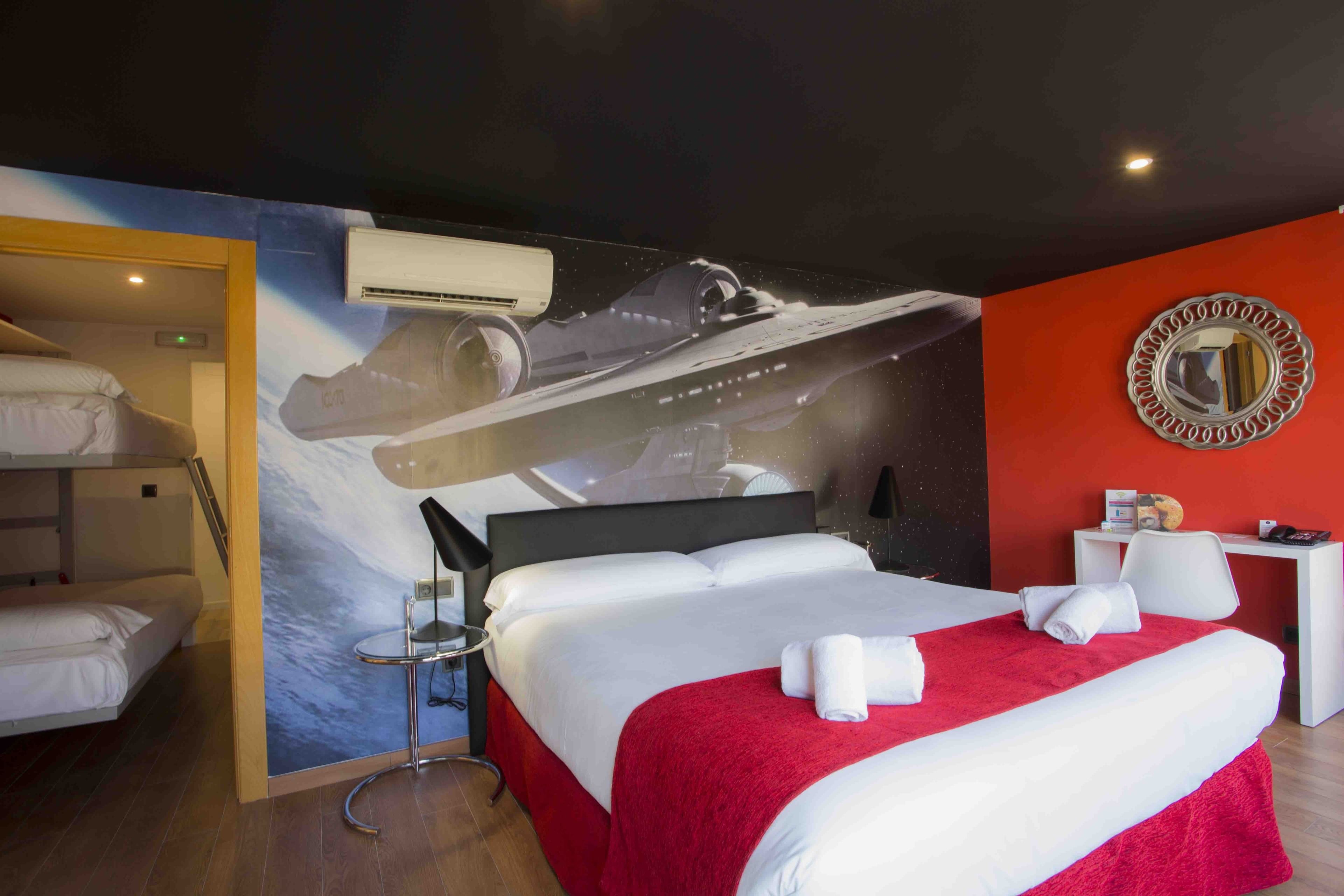 Habitació d'hotel amb un llit gran, una paret vermella decorativa, un mirall rodó i un aire condicionat fixat a la paret.