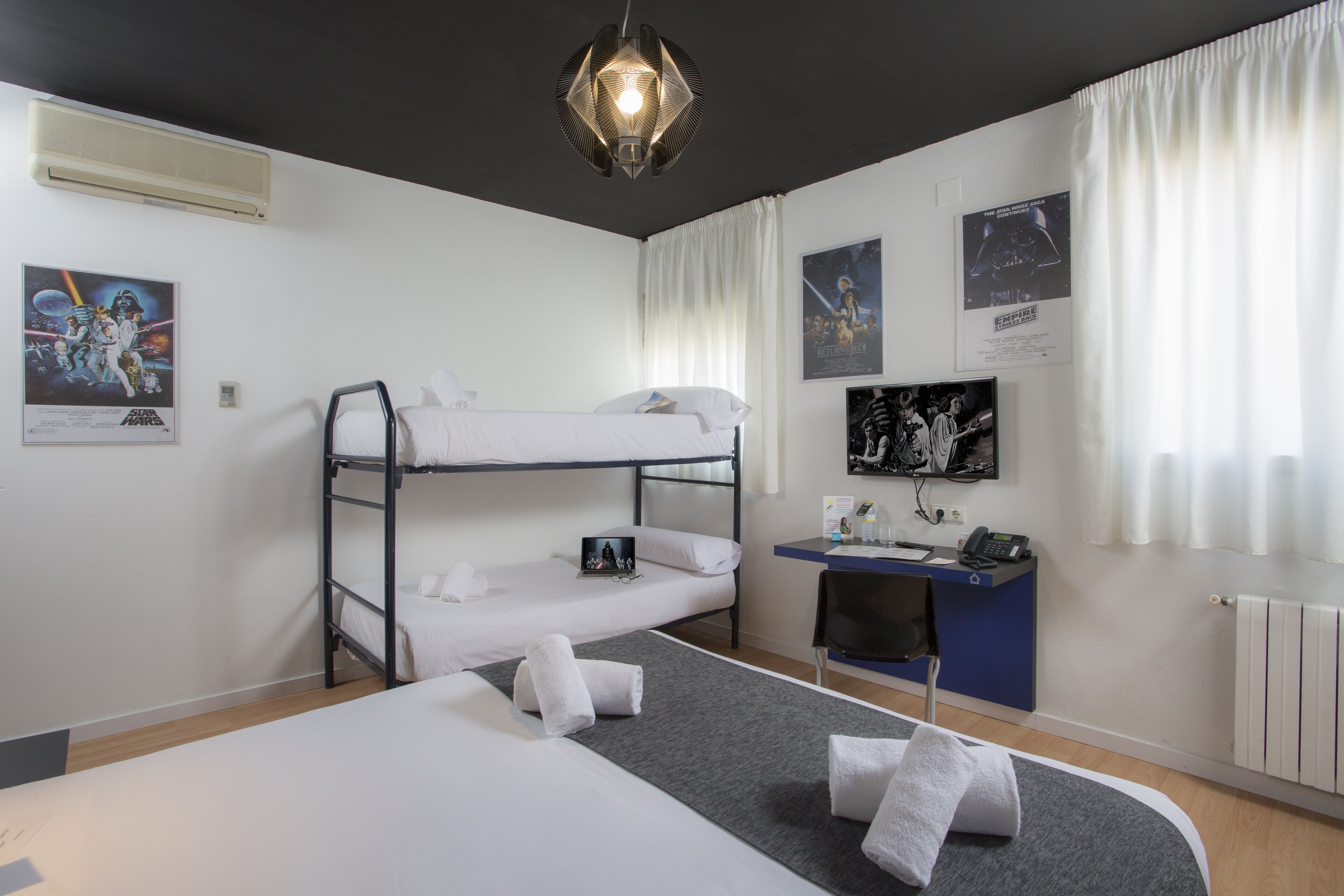 A bunk bed room with a desk, a chair, a TV, and posters on the wall.