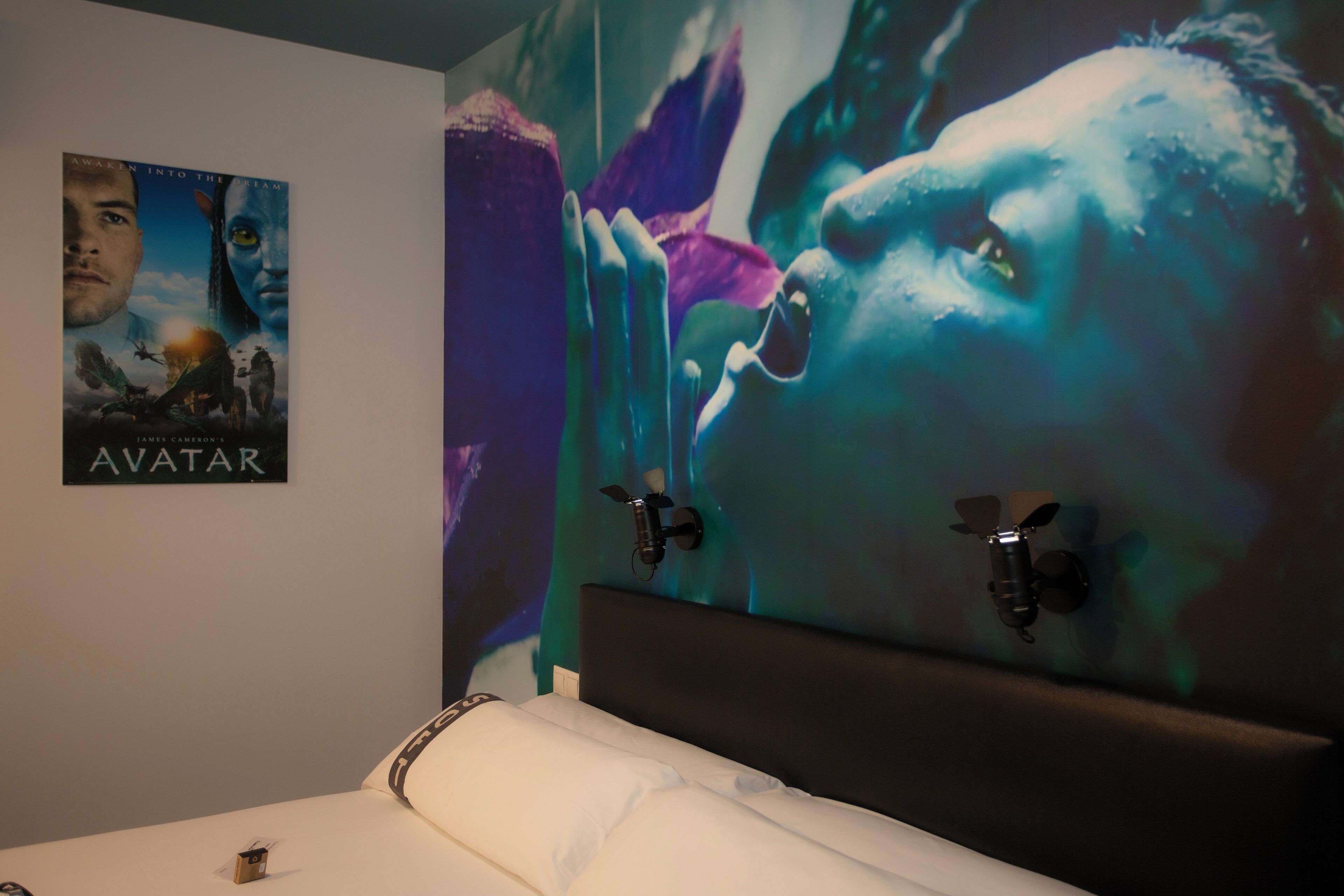 A bedroom with a large poster of Avatar, a bed with white bedding, and a headboard with a black panel.