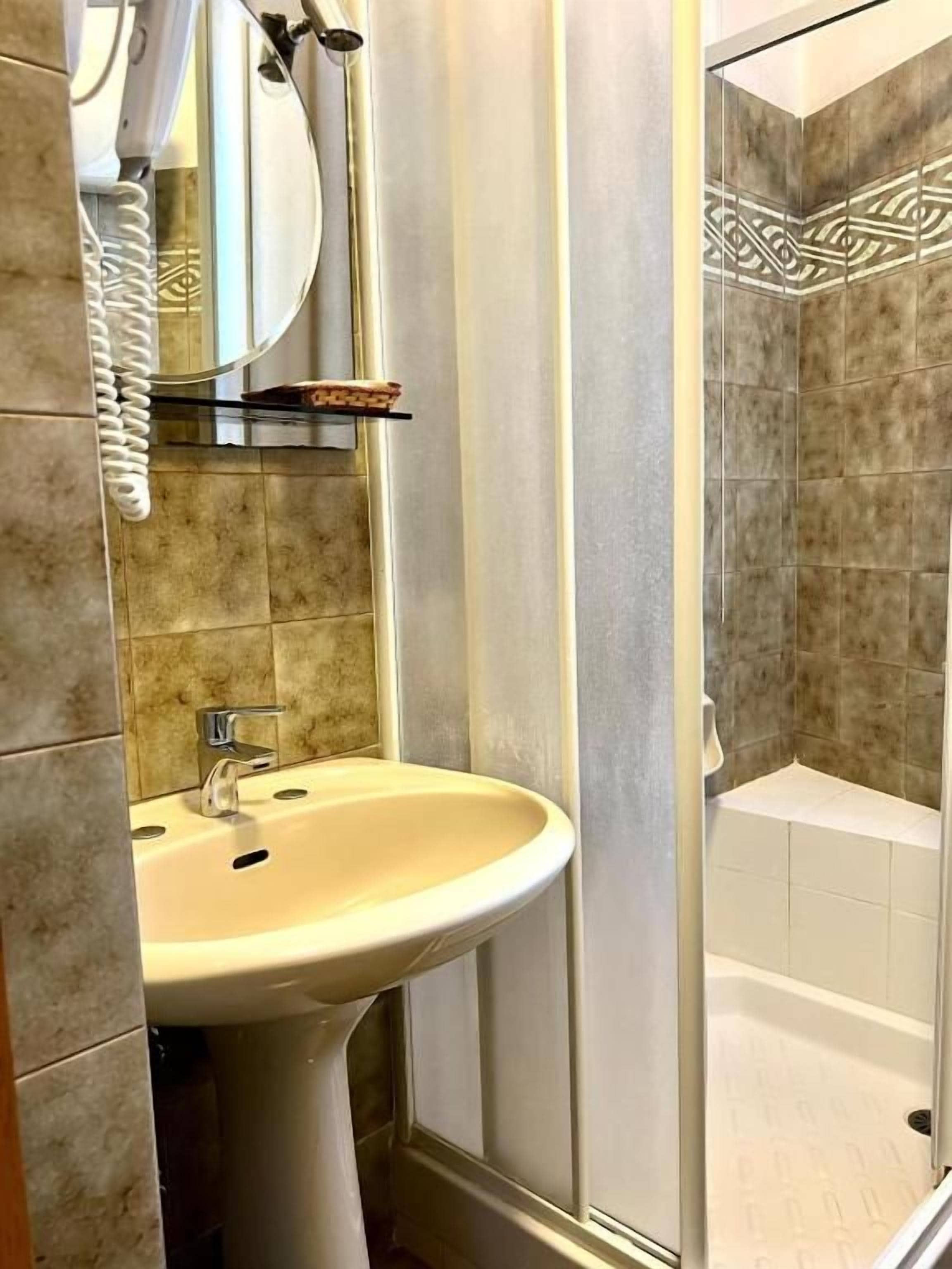 Un baño con lavamanos, espejo, ducha y paredes con azulejos.