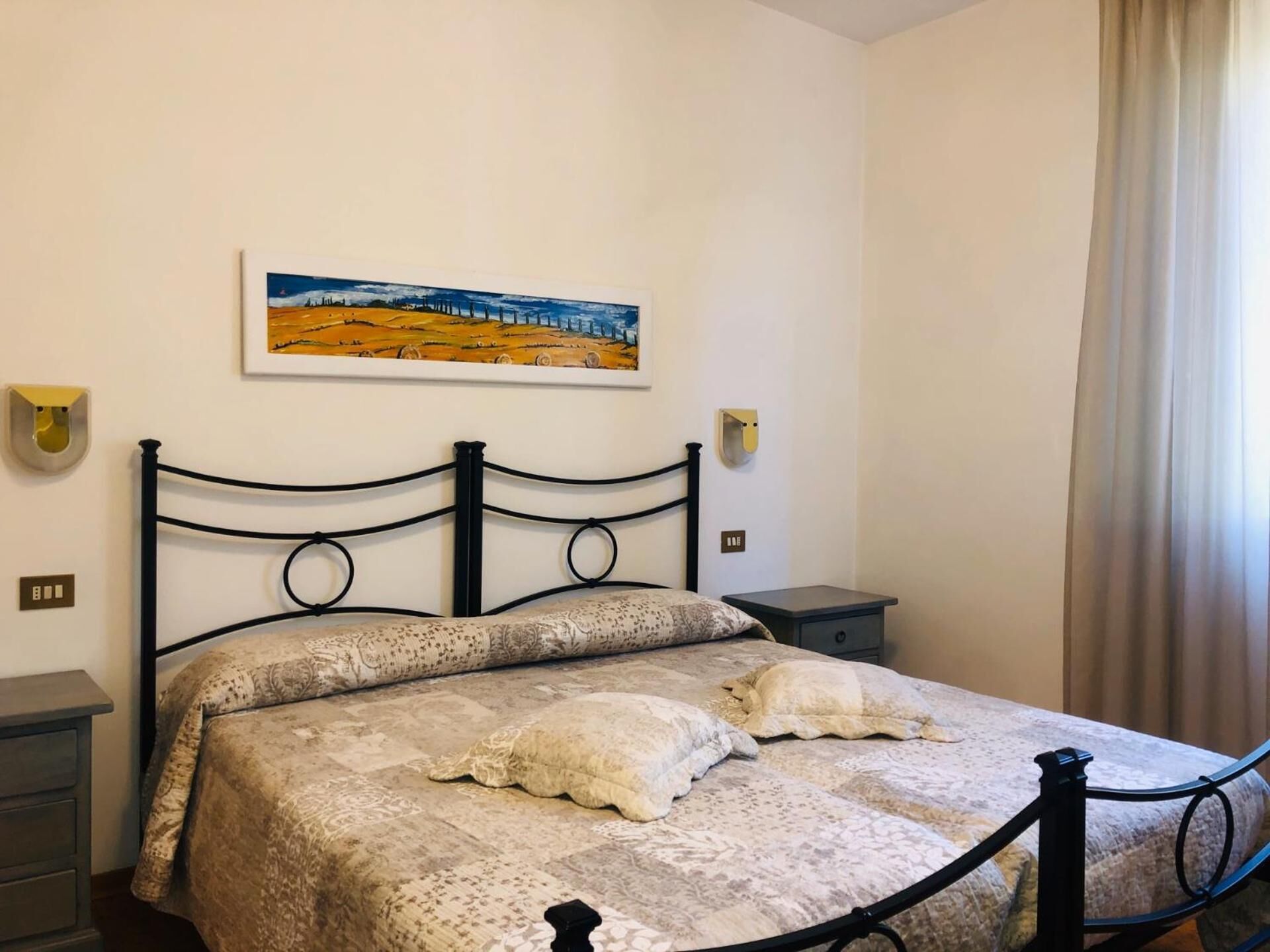Un dormitorio con una cama, una mesita de noche, una lámpara de pared y un cuadro.
