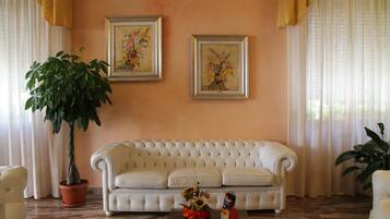 A living room with a white tufted sofa, two framed floral paintings on the wall, a potted plant, and a coffee table with a vase of flowers.