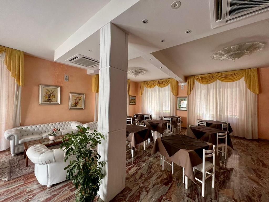 Una camera d'albergo con un'area soggiorno, tavoli da pranzo e una pianta grande.