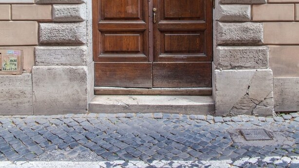 A double wooden door with a stone archway and a metal grille above it. - Rifugio Degli Artisti (Rome)