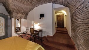 A room with a brick ceiling, a bed, a desk with a chair, and a staircase leading to another room. - Rifugio Degli Artisti (Rome)