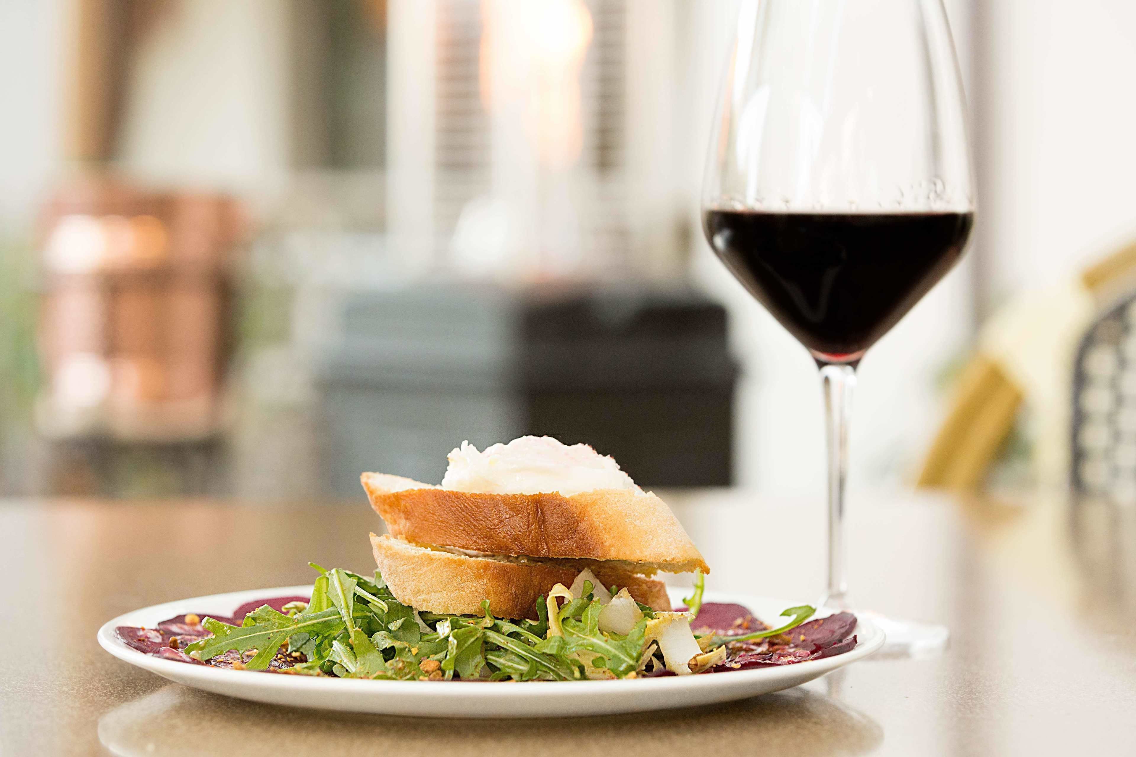 A plate with a sandwich and salad, and a glass of red wine on a table.