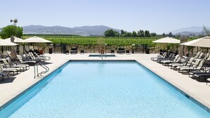 A pool with lounge chairs and umbrellas, surrounded by a fence, with a vineyard and mountains in the background. - Ponte Vineyard Inn (Temecula)