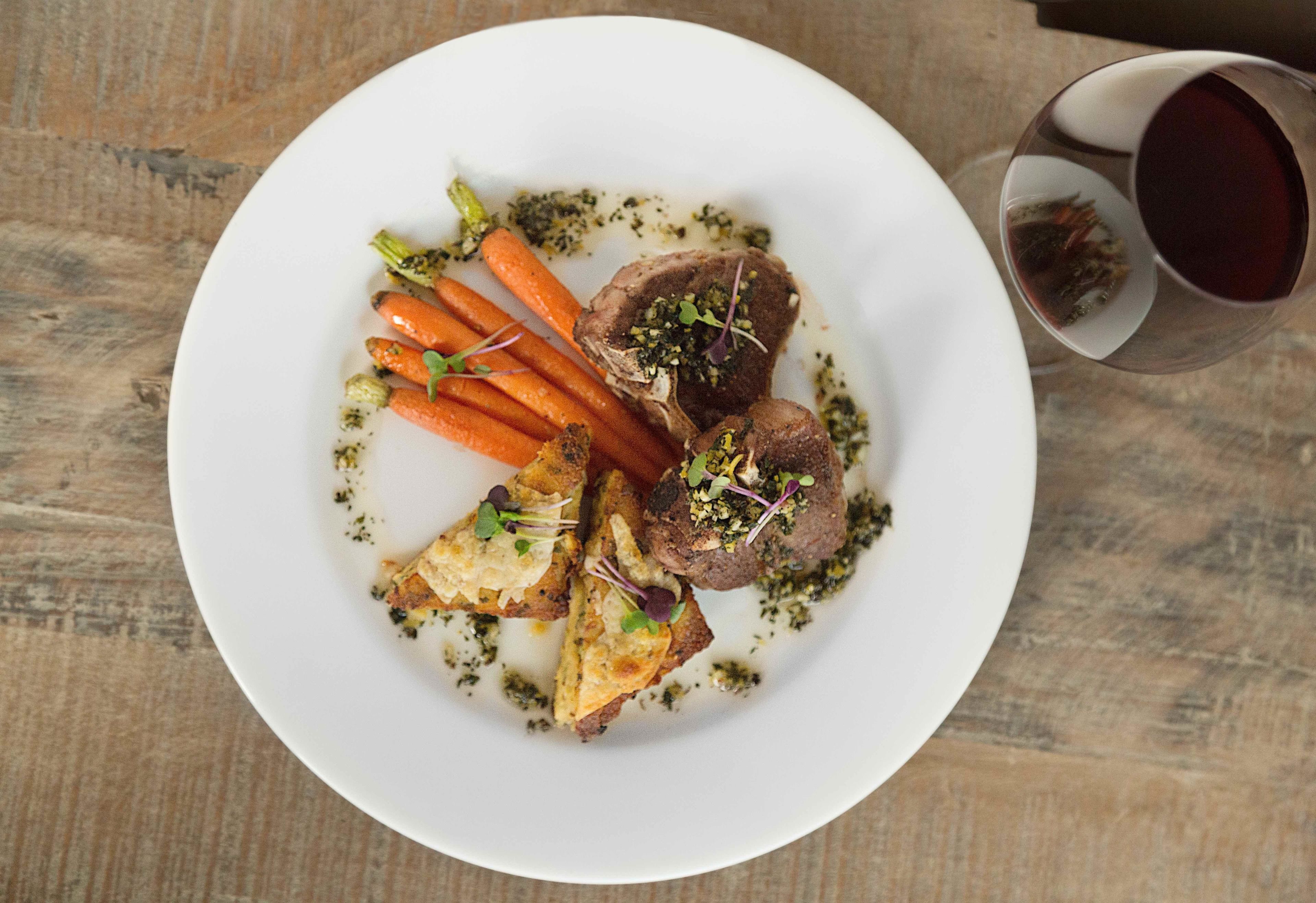 Une assiette de viande, de carottes et un verre de vin rouge.