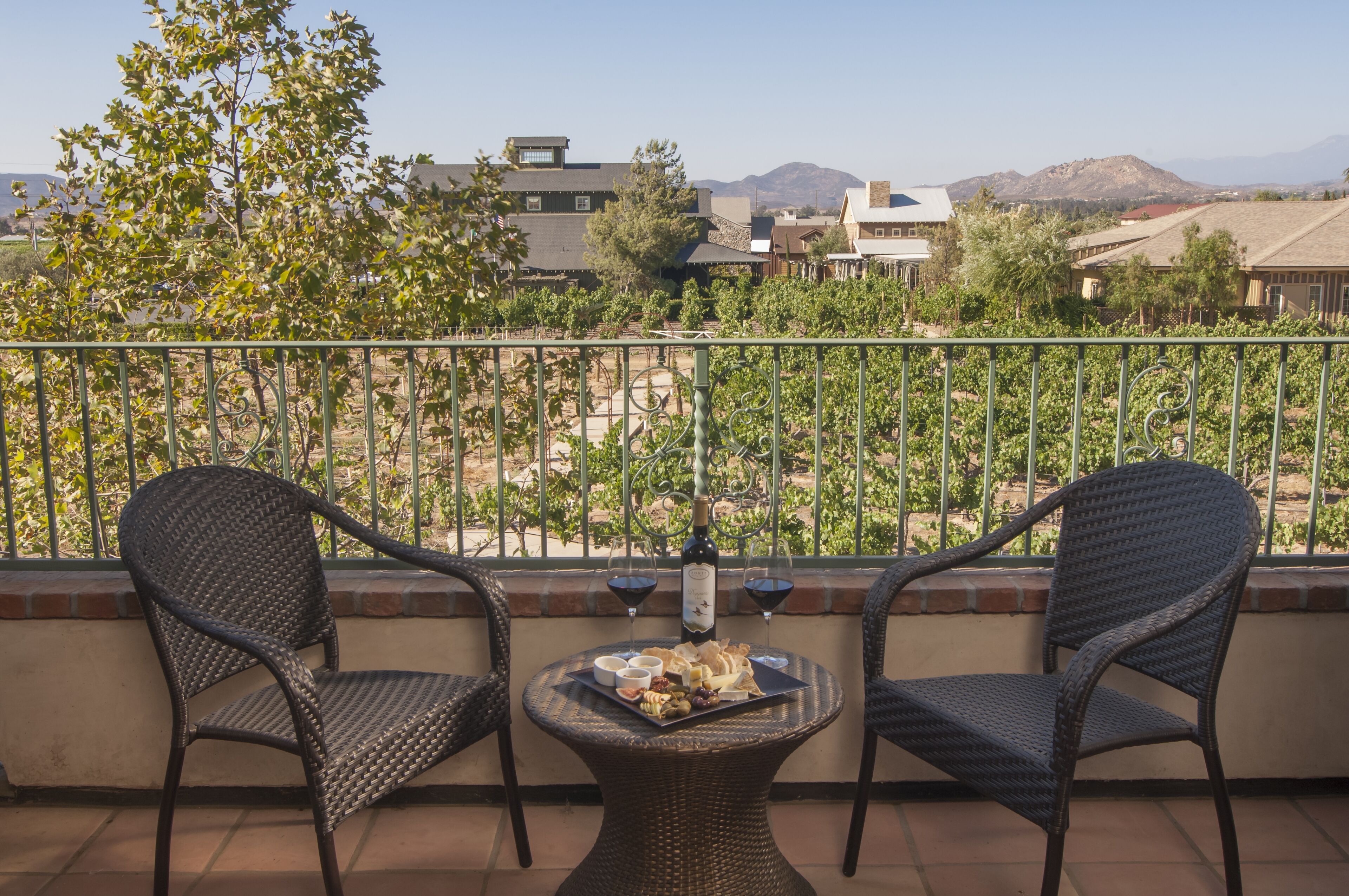 A balcony with two wicker chairs, a small table with a bottle and glasses, and a tray of food.