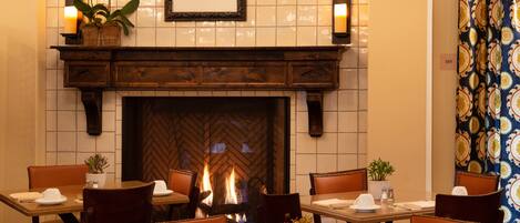 A dining area with a fireplace, wooden furniture, and potted plants.