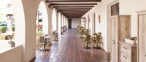 A corridor with tiled flooring, wooden chairs, and tables arranged along the sides.