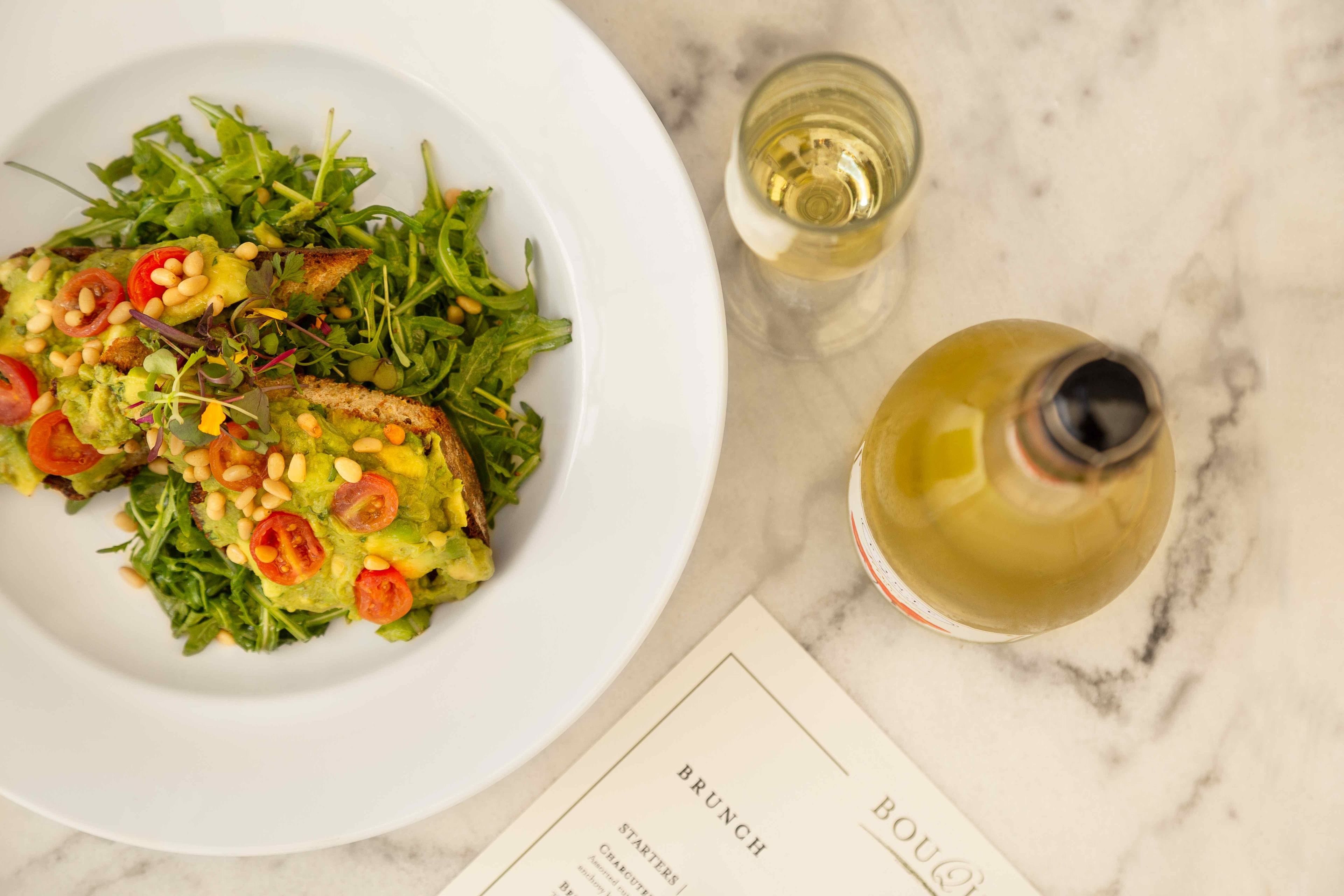 Um prato branco com salada e dois copos de vinho branco sobre uma superfície de mármore.