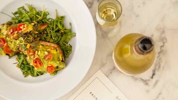 Um prato branco com salada e dois copos de vinho branco sobre uma superfície de mármore.