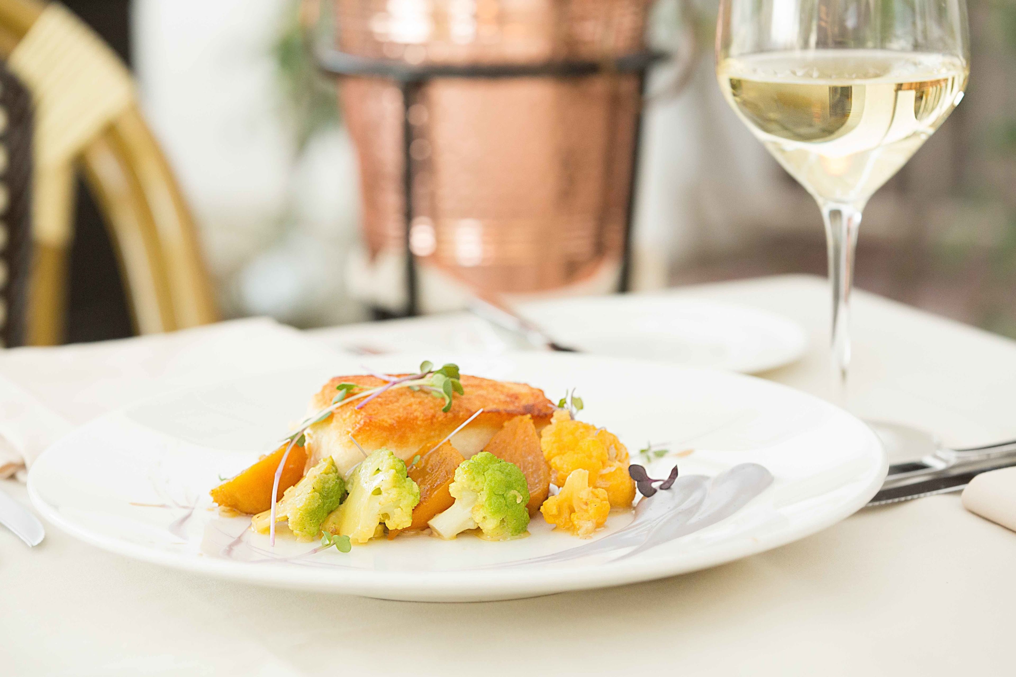A plate of food with a glass of white wine on a table.