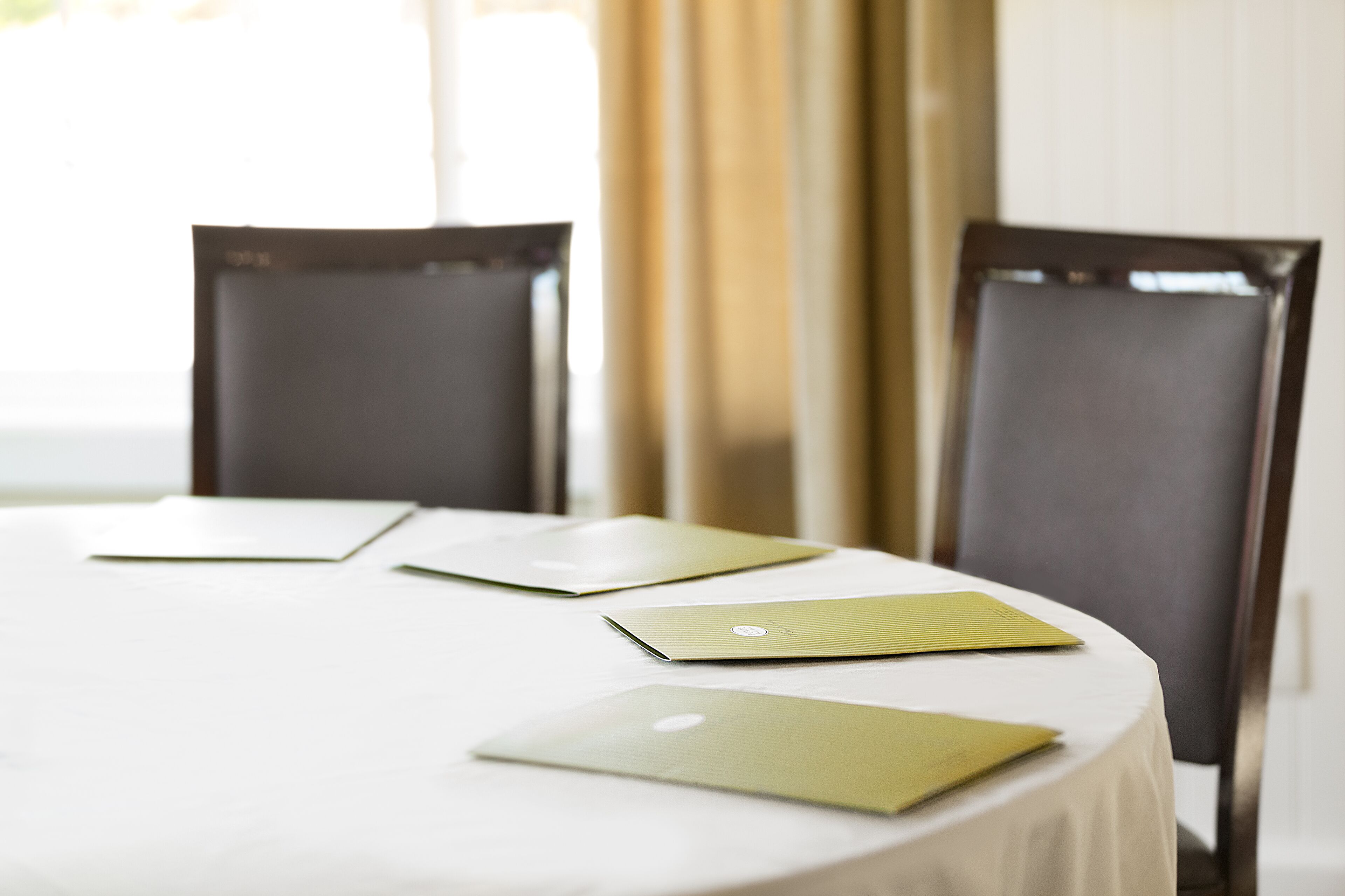 A round table with a white tablecloth, three laptops, and two dark chairs.